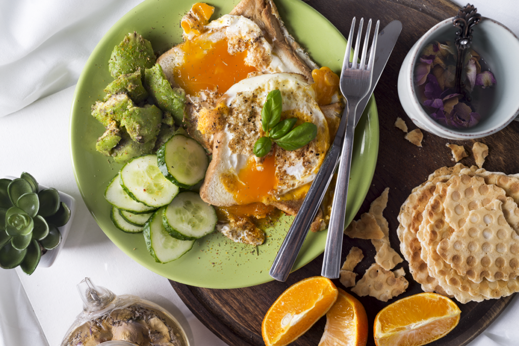 Healthy breakfast with avocado toast, fried eggs, and fresh vegetables