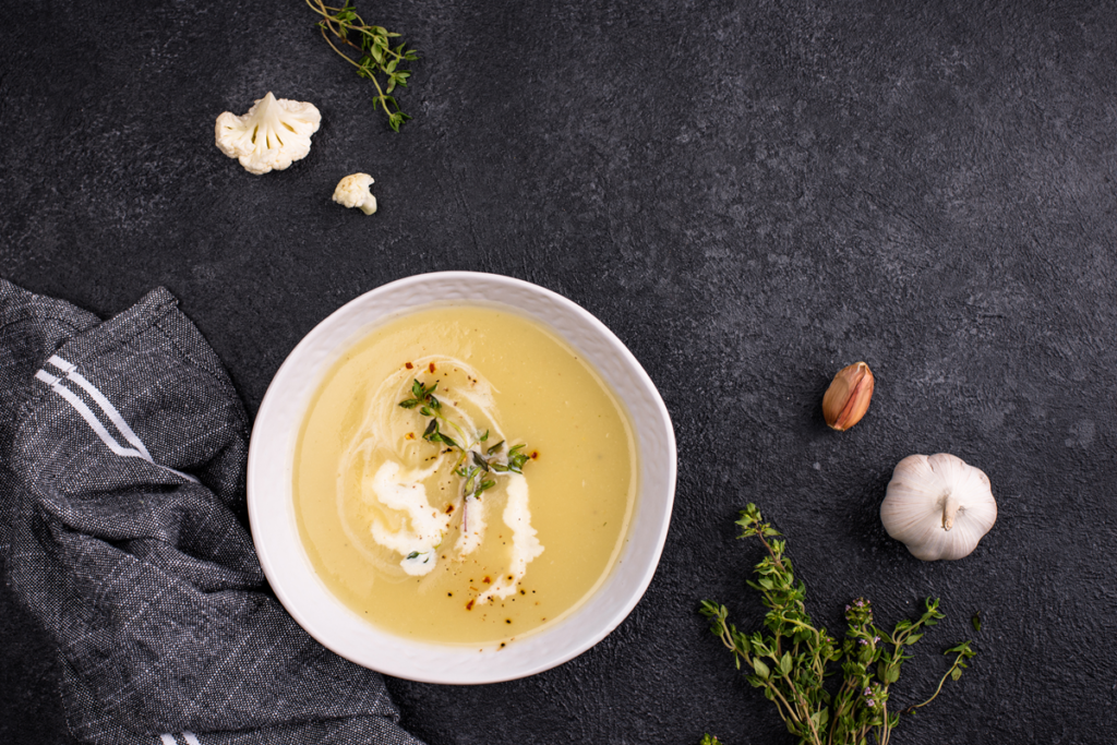 Bowl of roasted garlic cheddar cauliflower soup garnished with fresh herbs