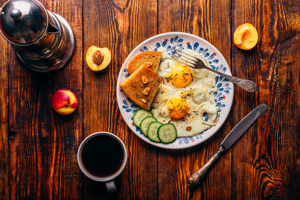 Toast with fried eggs on whole grain bread, topped with avocado and herbs, perfect for a healthy breakfast.