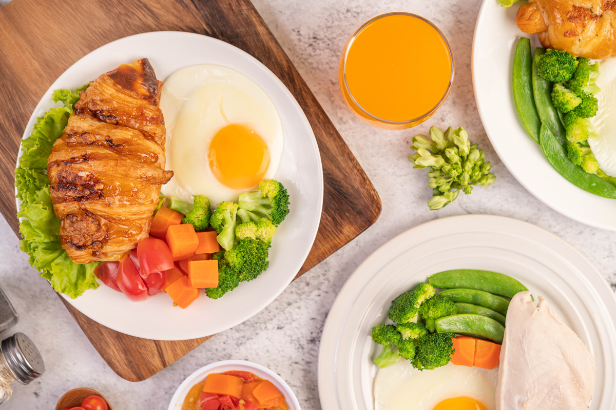 A balanced breakfast plate with chicken, fried eggs, broccoli, carrots, tomatoes, and lettuce.