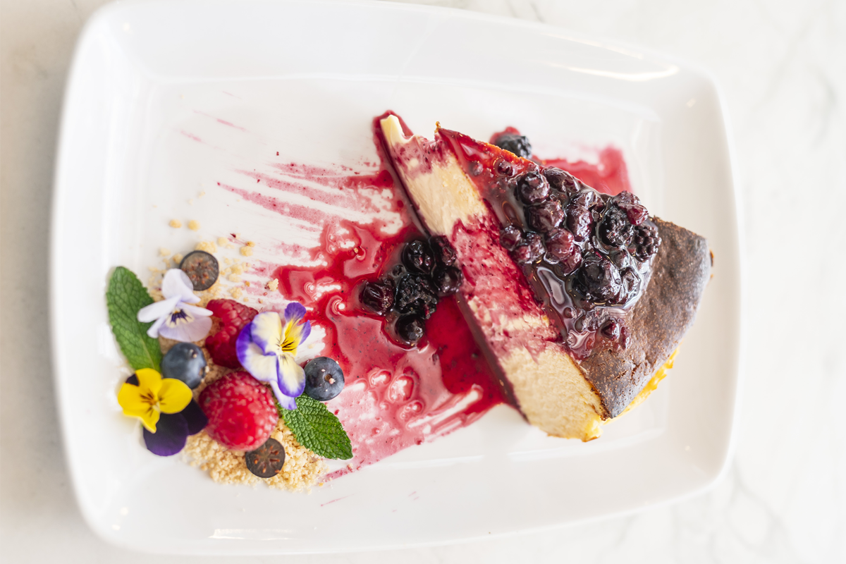 A slice of burnt cheesecake topped with fresh mixed berries and a caramelized top, showcasing its creamy interior.