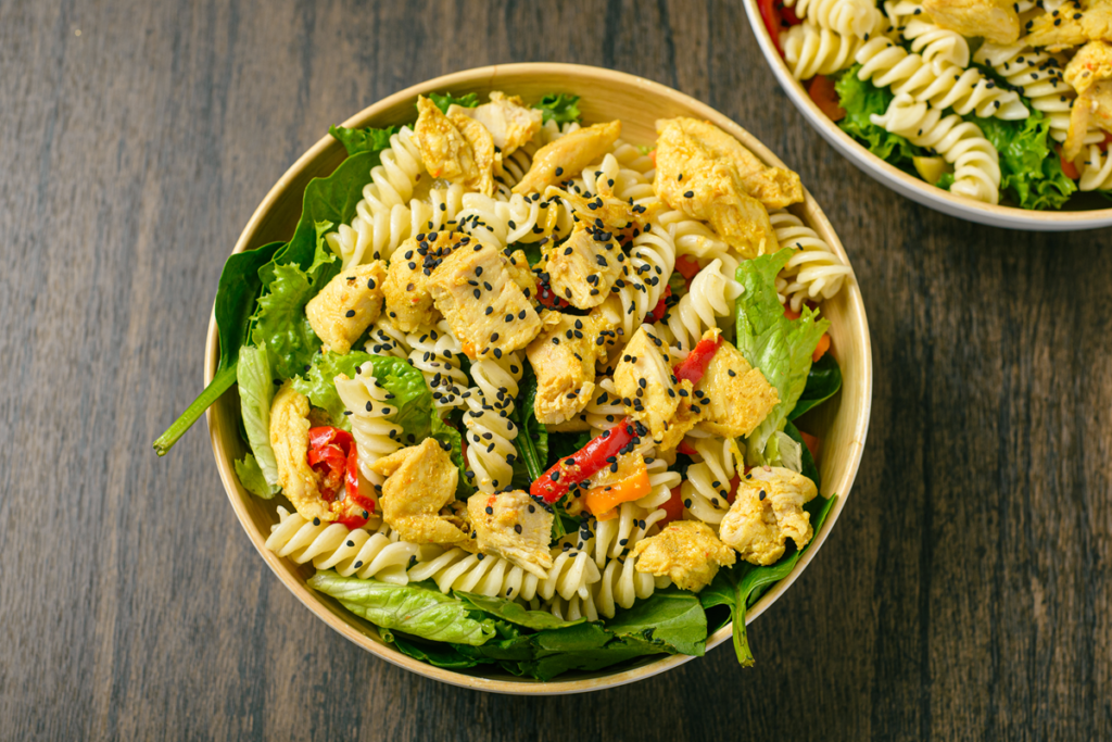 A vibrant bowl of Chicken Caesar Pasta Salad with grilled chicken, bowtie pasta, romaine lettuce, cherry tomatoes, and croutons.