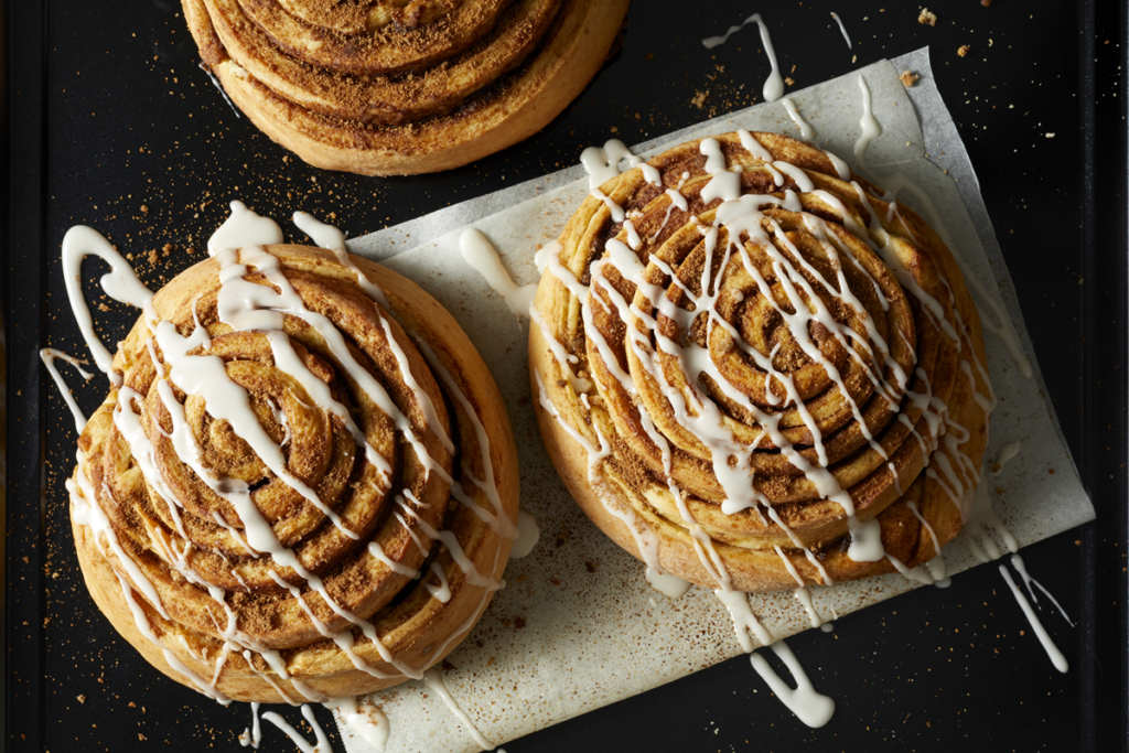 A batch of freshly baked cinnamon roll cookies with cream cheese frosting drizzle.