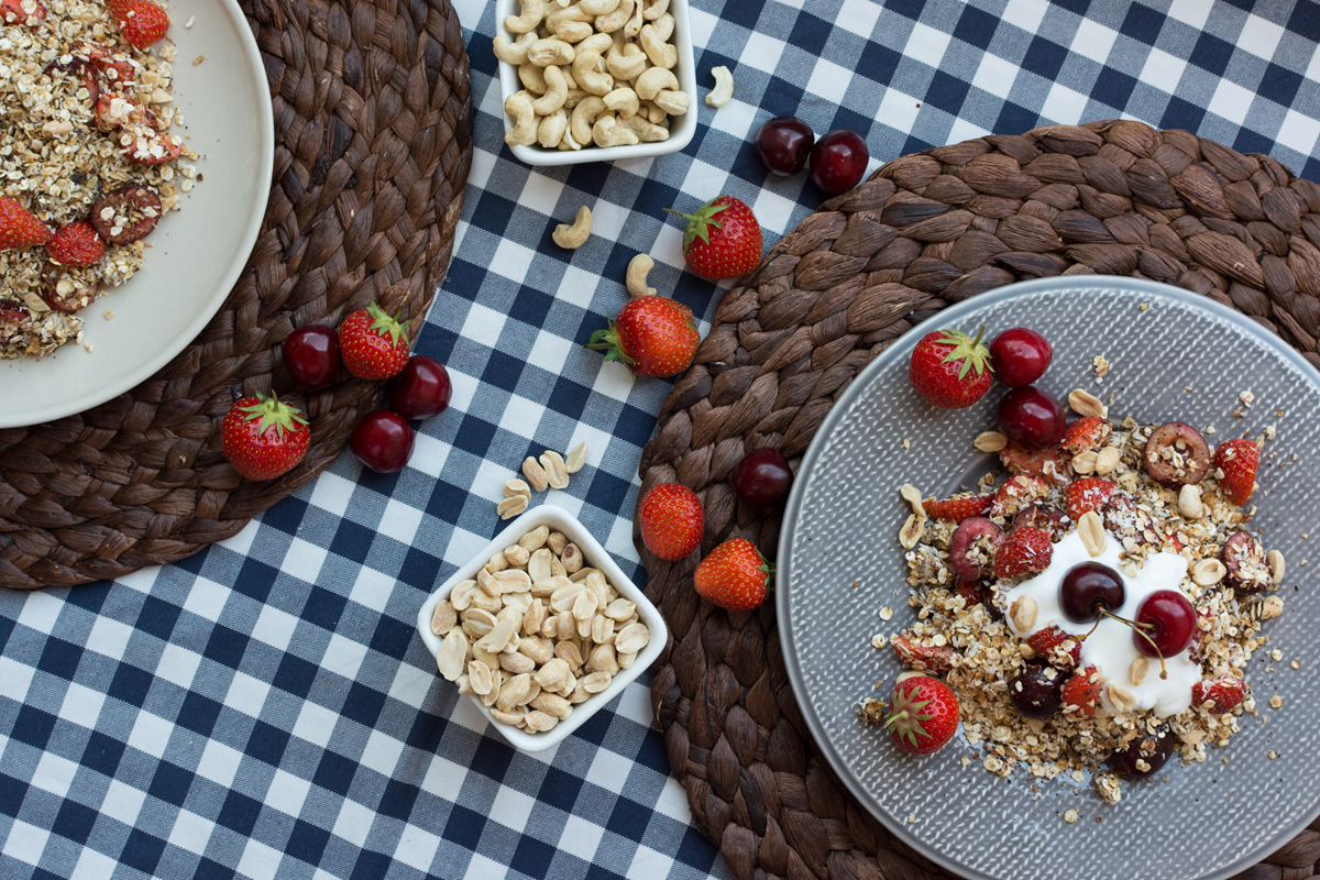 Bowl of homemade granola with cherries and yogurt on a checkered tablecloth