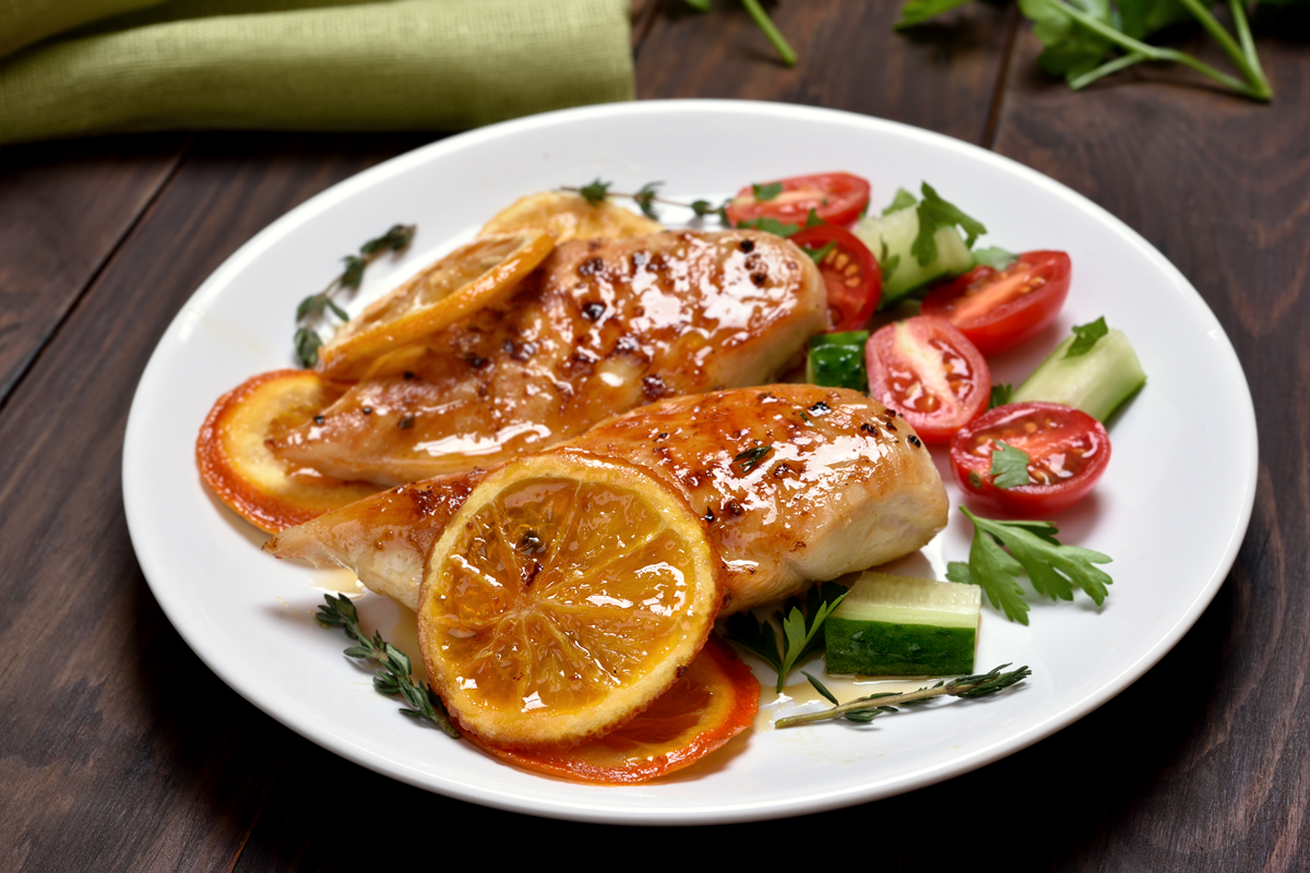 Roasted chicken breast with orange sauce garnished with fresh herbs.