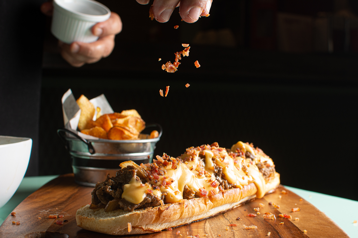 A cheesy garlic bread Sloppy Joe sandwich topped with bacon bits on a wooden board.