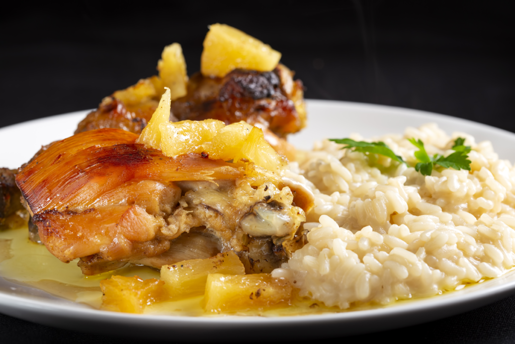 Chicken with pineapple and creamy rice served on a white plate.