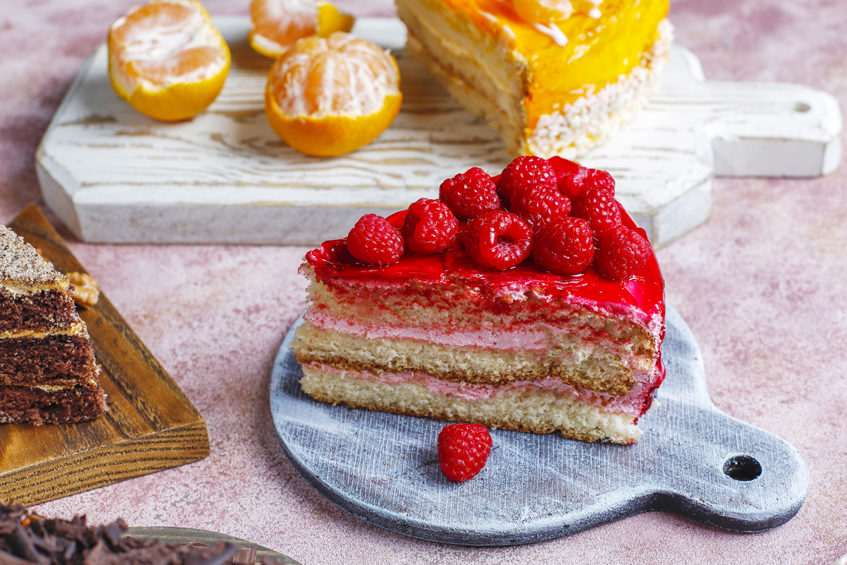 Slice of raspberry cake topped with fresh raspberries and a red glaze.