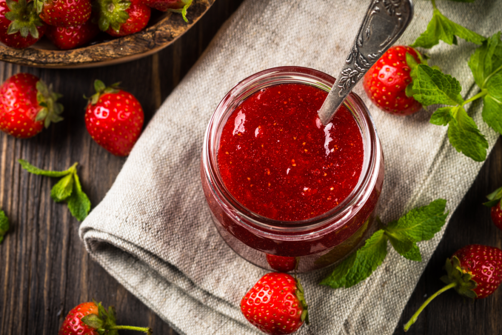 Jar of homemade strawberry jam with fresh strawberries and mint leaves