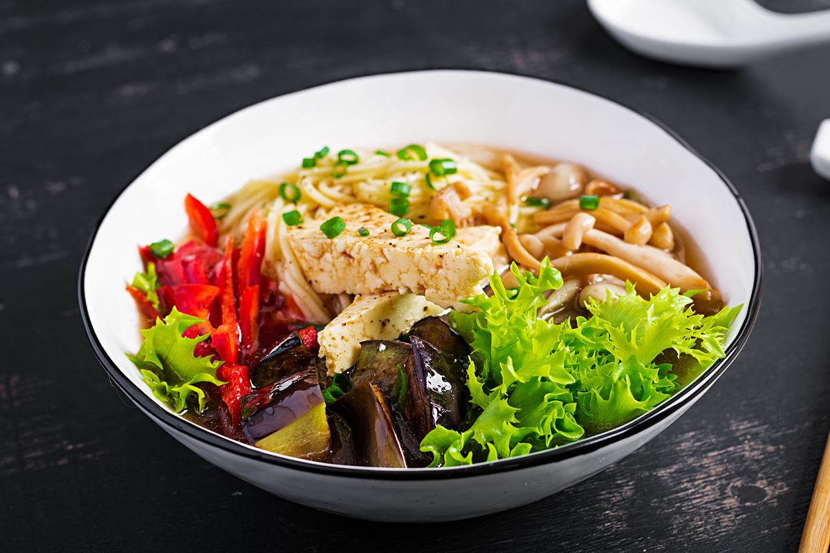 Bowl of Asian vegan noodle soup with tofu, mushrooms, and fresh vegetables.