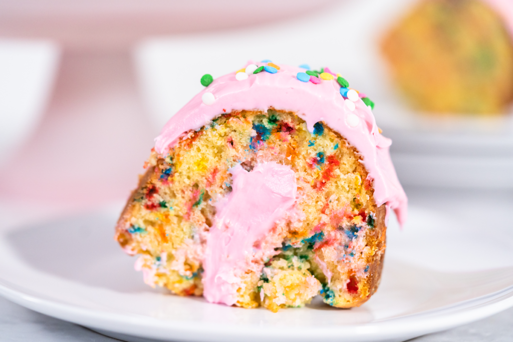 Slice of Funfetti Bundt Cake with pink frosting and colorful sprinkles.