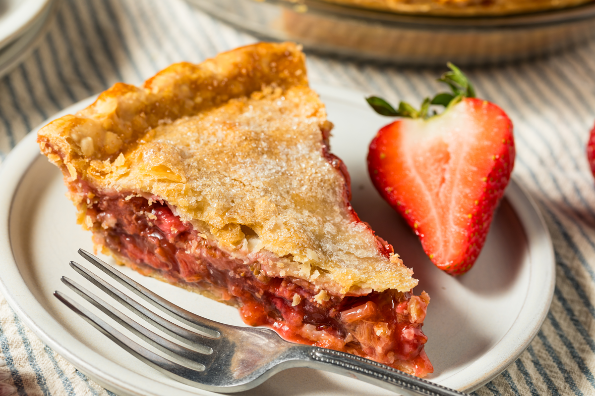 A slice of homemade strawberry rhubarb pie on a plate with a fresh strawberry